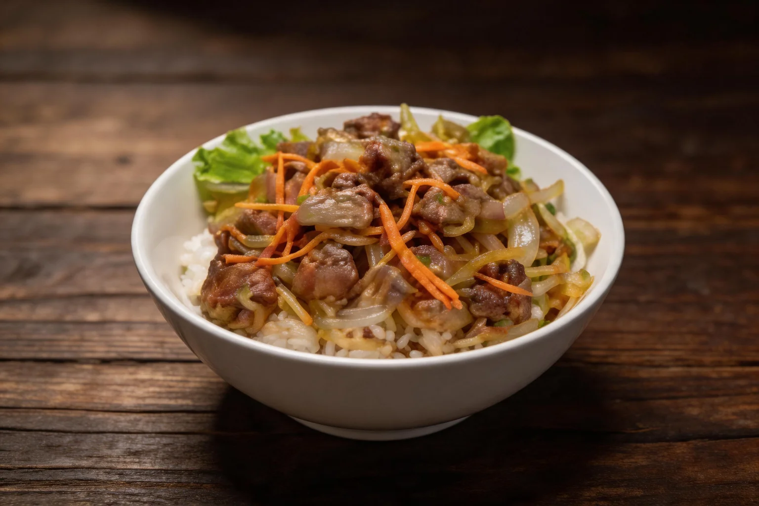 A white bowl of rice topped with beef sautéed with onions and julienned carrots, with a lettuce leaf